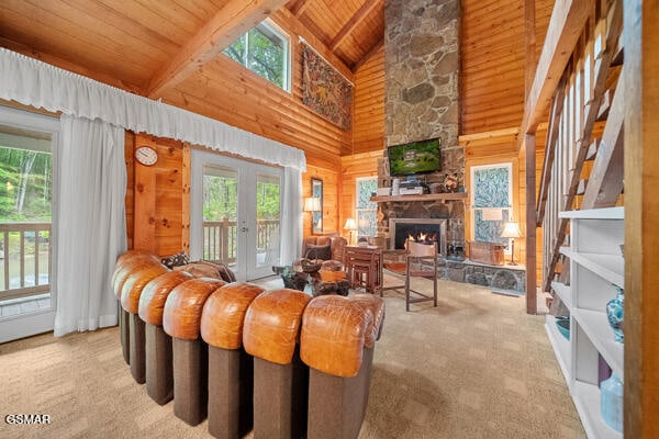 living area with french doors, lofted ceiling with beams, wooden walls, a stone fireplace, and wooden ceiling