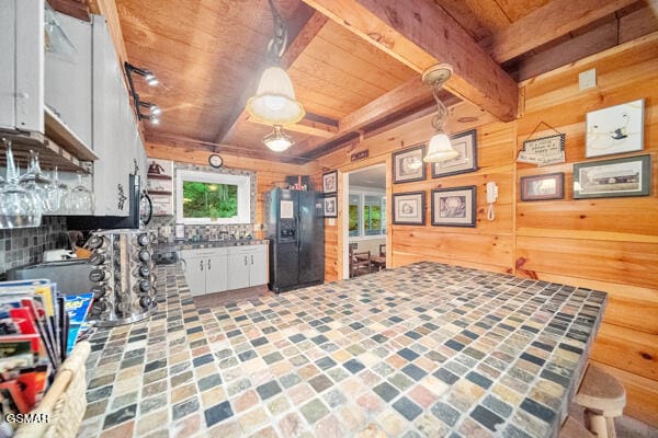 kitchen with wood ceiling, white cabinets, wood walls, beamed ceiling, and black fridge