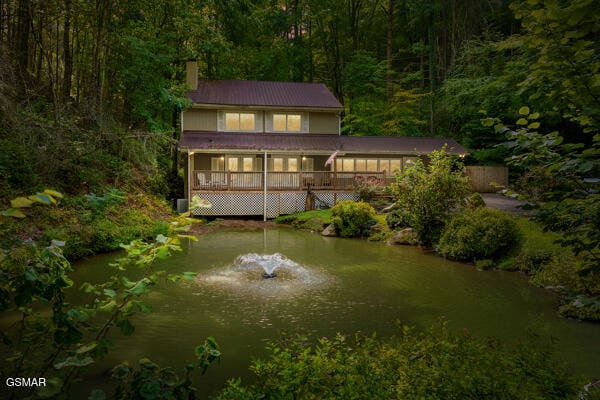 back of property with a chimney, a water view, and a view of trees