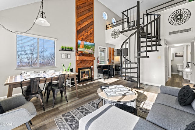 living area with baseboards, visible vents, a glass covered fireplace, stairway, and wood finished floors