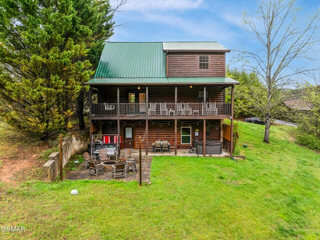 rear view of house featuring faux log siding, a hot tub, an outdoor fire pit, a patio area, and a lawn