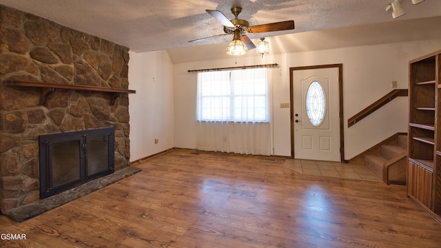 foyer entrance with hardwood / wood-style flooring, ceiling fan, a fireplace, and a textured ceiling