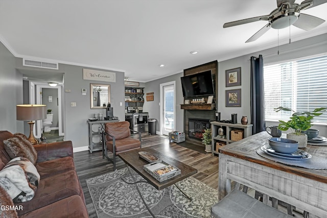 living room featuring ceiling fan, a fireplace, dark hardwood / wood-style flooring, and crown molding