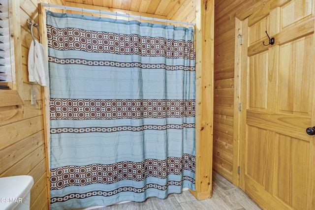 full bath featuring curtained shower, toilet, and wooden walls