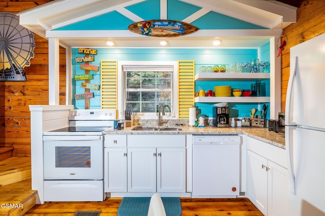 kitchen featuring wood walls, light stone countertops, a sink, and white appliances