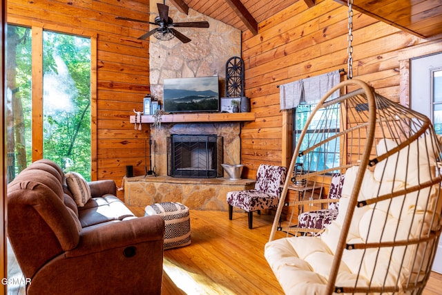 living room with wood walls, wood finished floors, a stone fireplace, vaulted ceiling with beams, and wooden ceiling