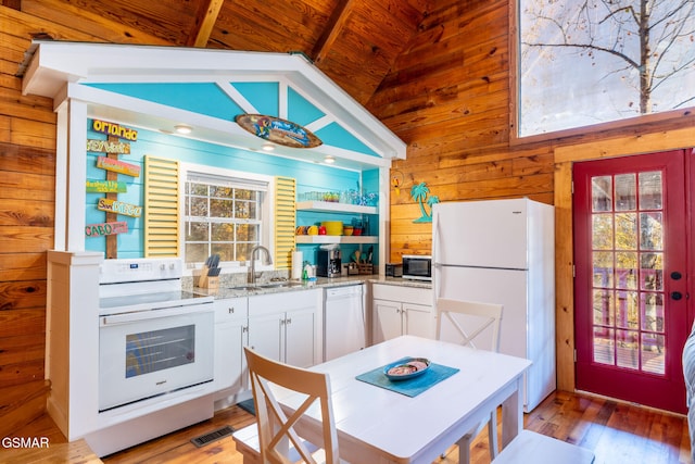 kitchen with plenty of natural light, wooden walls, visible vents, white appliances, and lofted ceiling with beams