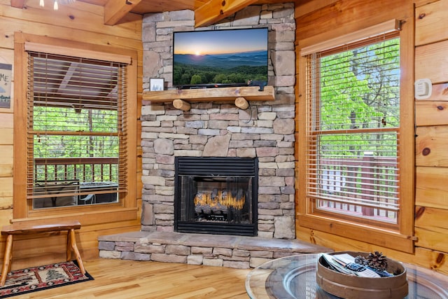 living room with hardwood / wood-style flooring, a stone fireplace, and wooden walls