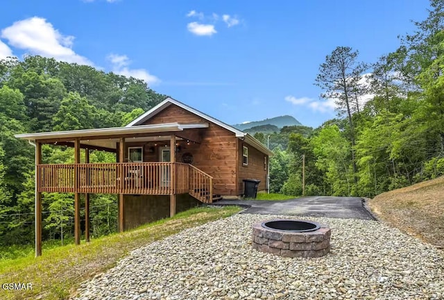 back of property with a deck with mountain view and an outdoor fire pit