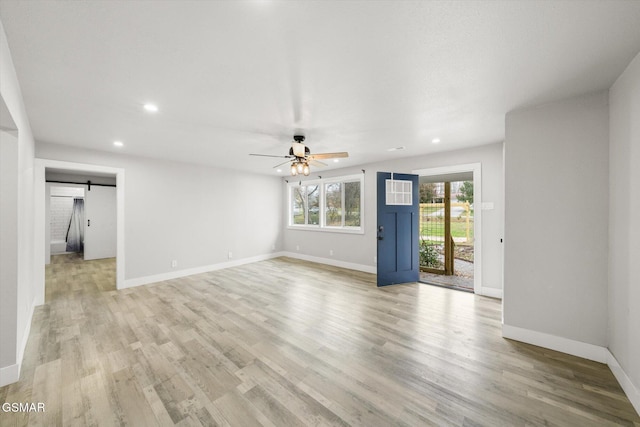 unfurnished living room featuring a barn door, ceiling fan, and light wood-type flooring