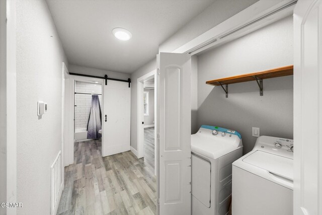 washroom with washing machine and clothes dryer, a barn door, and light hardwood / wood-style floors