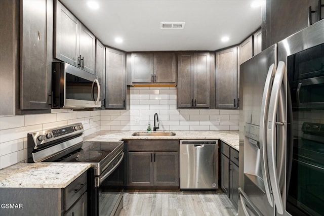 kitchen featuring light stone countertops, appliances with stainless steel finishes, dark brown cabinets, sink, and light hardwood / wood-style flooring