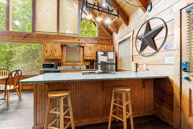 kitchen featuring appliances with stainless steel finishes, a sink, wood walls, wood finished floors, and light stone counters
