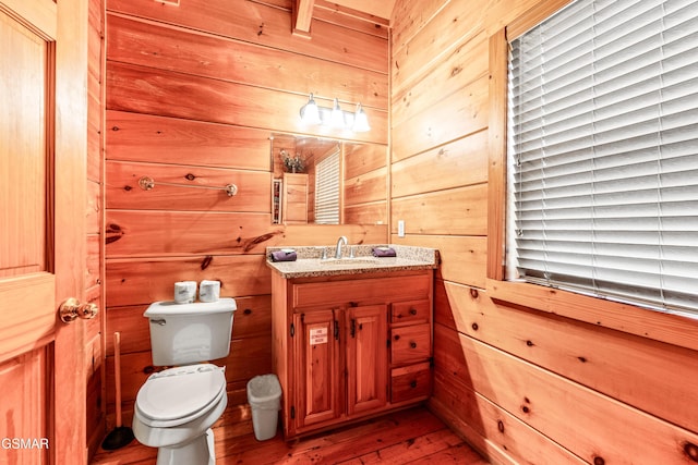 half bathroom with toilet, wood walls, vanity, and hardwood / wood-style floors