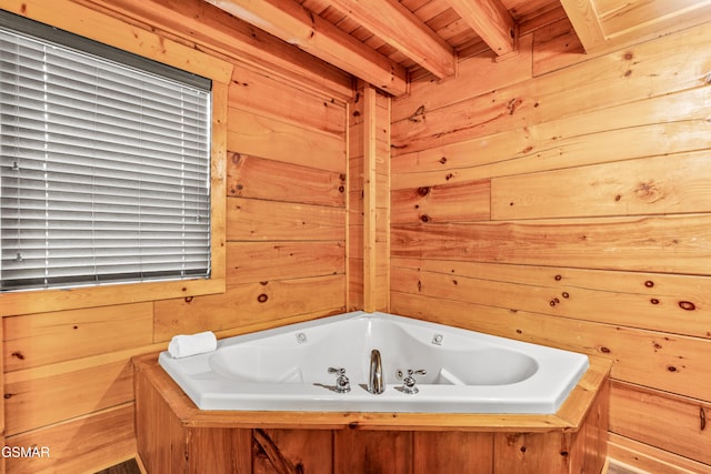 bathroom with wooden walls, wood ceiling, a tub with jets, and beamed ceiling