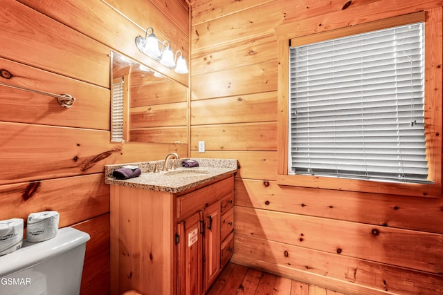 half bathroom featuring wood walls, vanity, toilet, and wood-type flooring