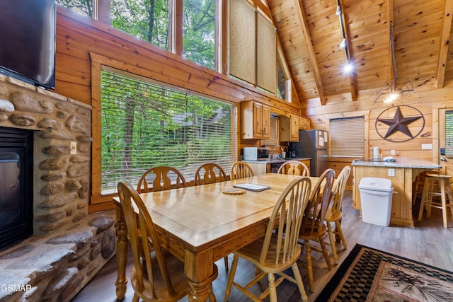 dining room with high vaulted ceiling, wood walls, a fireplace, light wood-style floors, and wood ceiling