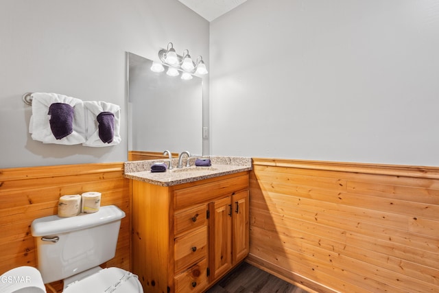 half bath with toilet, wood finished floors, and vanity