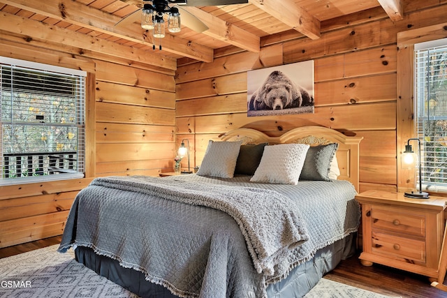 bedroom featuring wood ceiling, beamed ceiling, multiple windows, wood finished floors, and wooden walls
