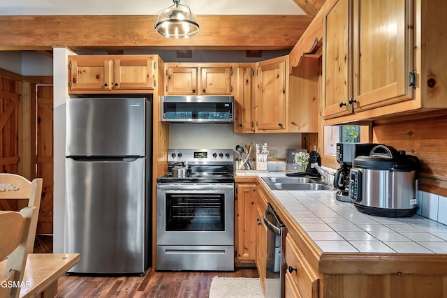 kitchen with appliances with stainless steel finishes, tile countertops, a sink, and dark wood finished floors