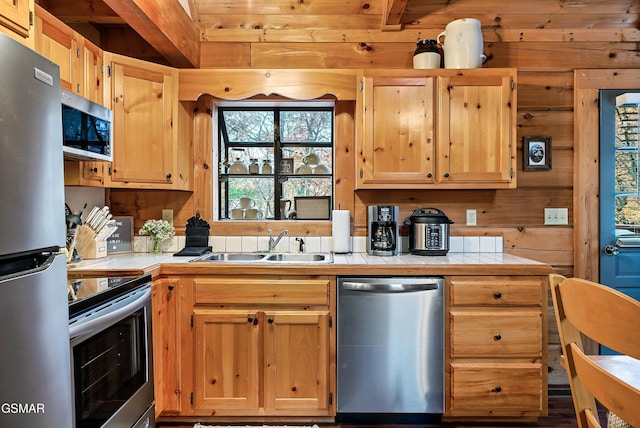 kitchen featuring appliances with stainless steel finishes, tile counters, a sink, wooden walls, and light brown cabinets