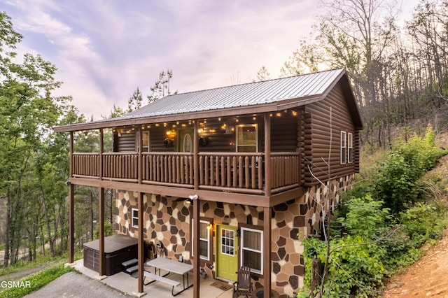 back of house featuring log siding, a patio area, stone siding, metal roof, and a balcony