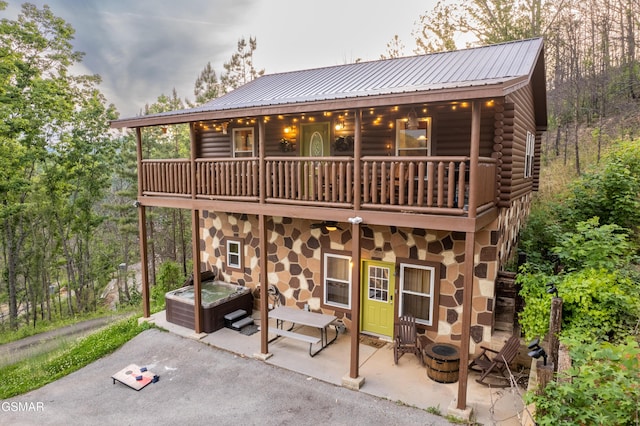 back of property with a hot tub, log siding, a patio area, stone siding, and a balcony