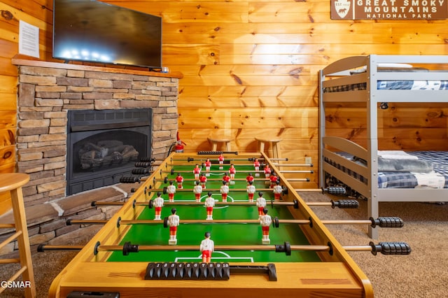 recreation room featuring wooden walls, a stone fireplace, and carpet