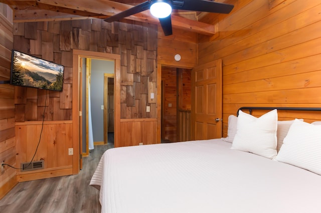 bedroom featuring wooden walls, beamed ceiling, and ceiling fan