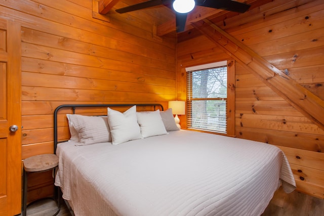 bedroom featuring beamed ceiling, hardwood / wood-style floors, ceiling fan, and wood walls