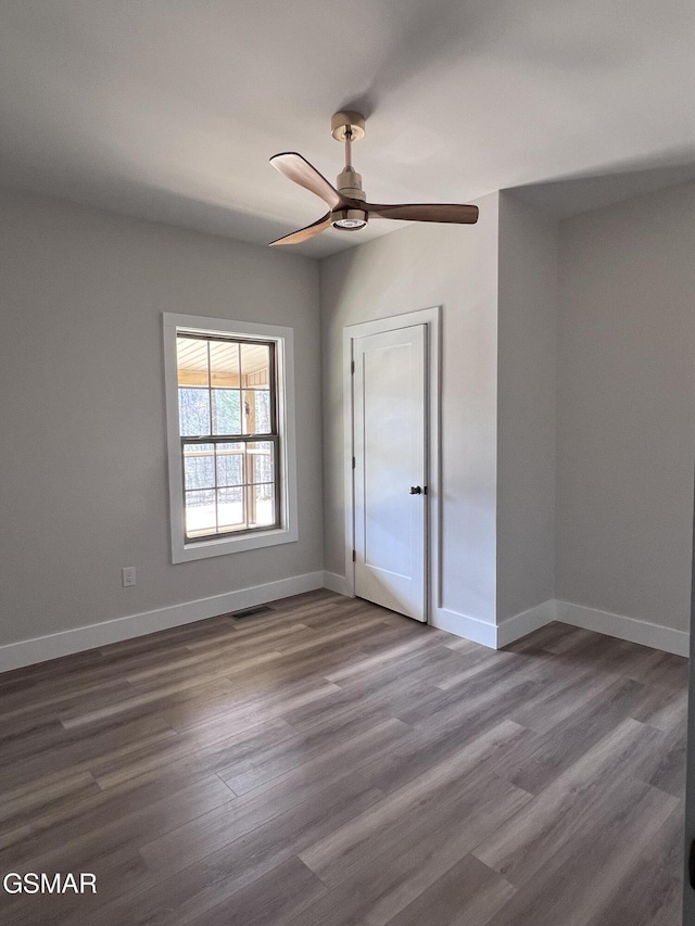 spare room with ceiling fan, visible vents, baseboards, and dark wood finished floors