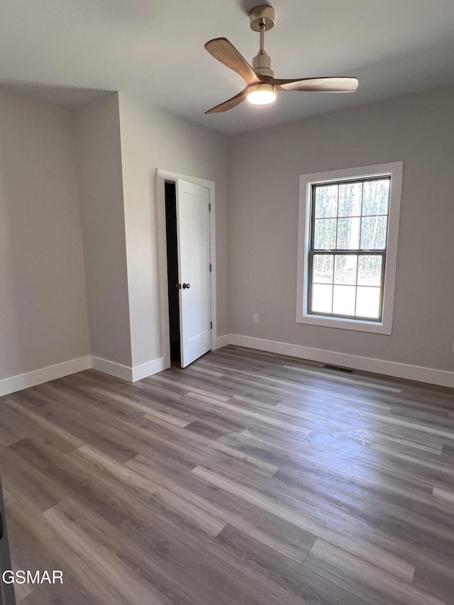 unfurnished room featuring ceiling fan, visible vents, baseboards, and wood finished floors