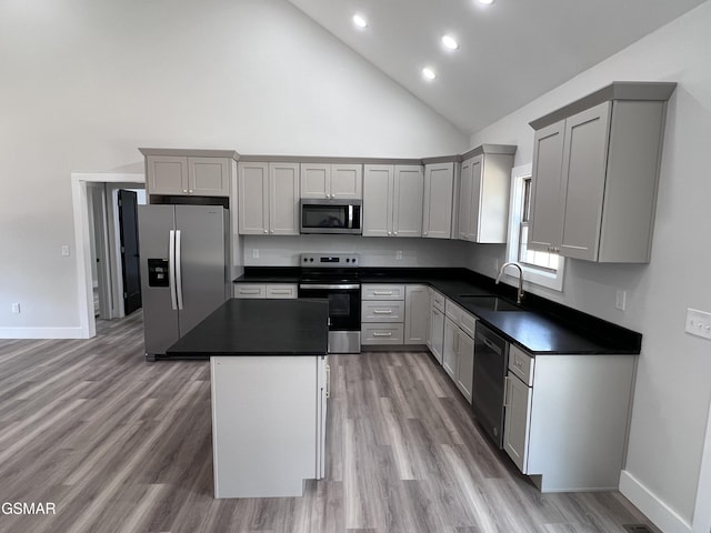 kitchen with a sink, a kitchen island, dark countertops, stainless steel appliances, and light wood-style floors