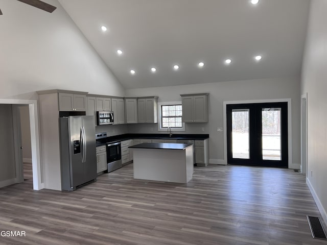 kitchen with visible vents, a kitchen island, a sink, stainless steel appliances, and dark countertops