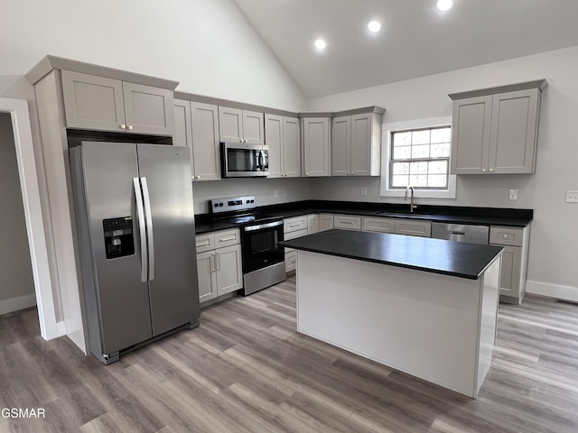 kitchen with light wood-type flooring, a sink, dark countertops, a kitchen island, and stainless steel appliances