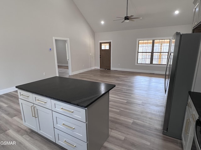 kitchen featuring light wood-style flooring, a kitchen island, dark countertops, white cabinetry, and freestanding refrigerator