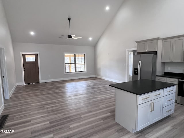 kitchen with dark countertops, light wood finished floors, baseboards, stainless steel refrigerator with ice dispenser, and high vaulted ceiling