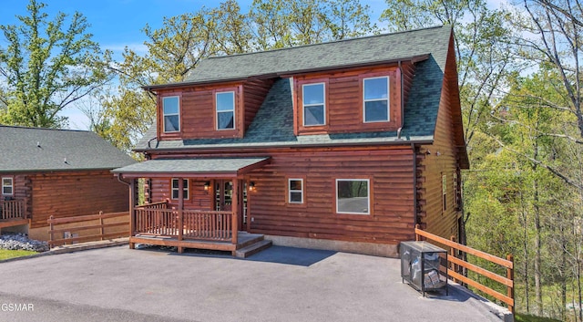 rear view of house featuring covered porch, roof with shingles, and log siding