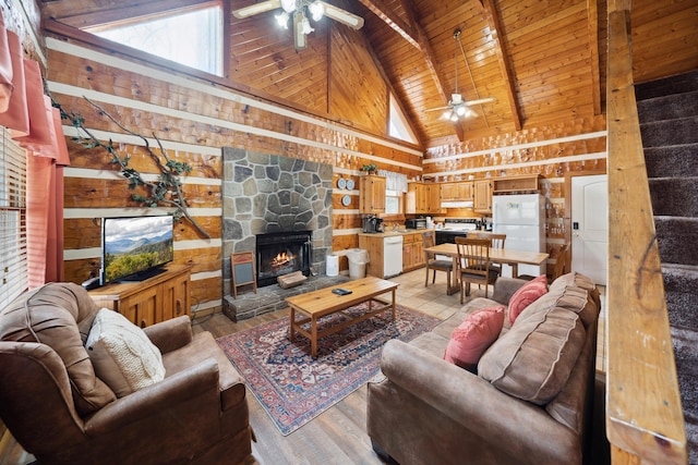 living room featuring beam ceiling, wood ceiling, a stone fireplace, light wood-type flooring, and ceiling fan