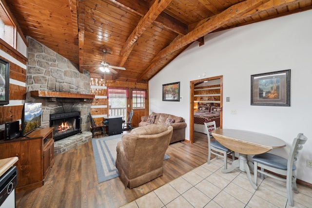 living area featuring wooden ceiling, beamed ceiling, ceiling fan, light wood-style flooring, and a stone fireplace