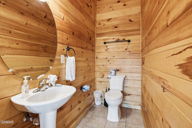 half bath featuring tile patterned floors, wood walls, toilet, and a sink