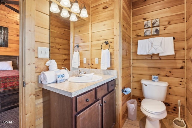 ensuite bathroom featuring toilet, wood walls, vanity, and tile patterned flooring