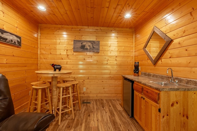 bar with dishwasher, sink, wooden ceiling, wood walls, and light hardwood / wood-style floors