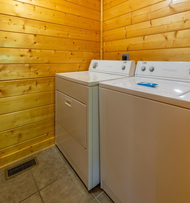 laundry room with wooden walls, light tile patterned floors, and independent washer and dryer