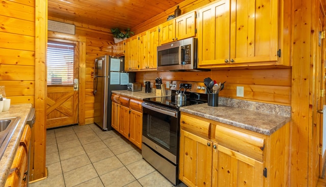 kitchen featuring light tile patterned floors, stainless steel appliances, wooden walls, and wooden ceiling