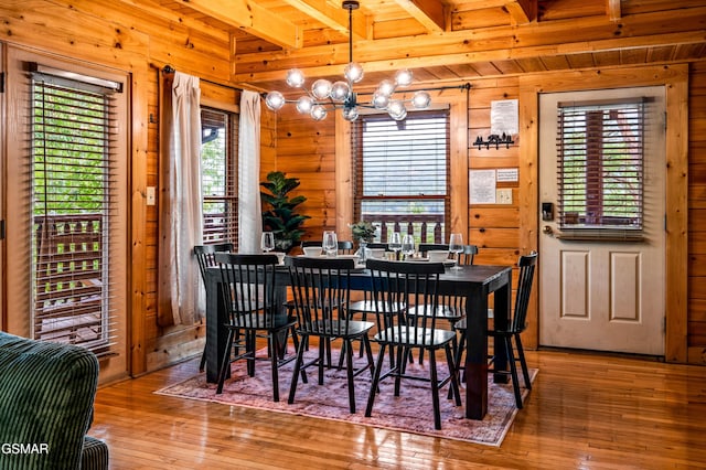 dining area with hardwood / wood-style flooring, wooden walls, beamed ceiling, and a chandelier