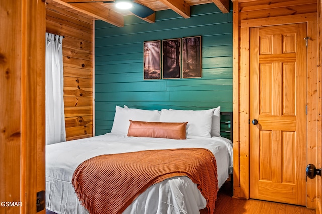 bedroom featuring beam ceiling, wood walls, and wood finished floors