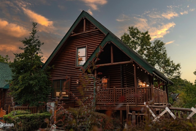 back of house at dusk featuring a wooden deck and log exterior