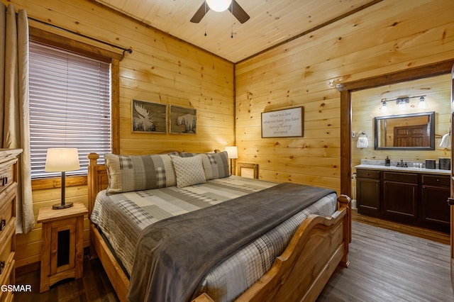 bedroom with connected bathroom, wooden walls, sink, hardwood / wood-style flooring, and ceiling fan