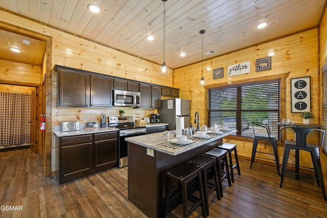 kitchen featuring appliances with stainless steel finishes, decorative light fixtures, an island with sink, a kitchen breakfast bar, and dark brown cabinetry